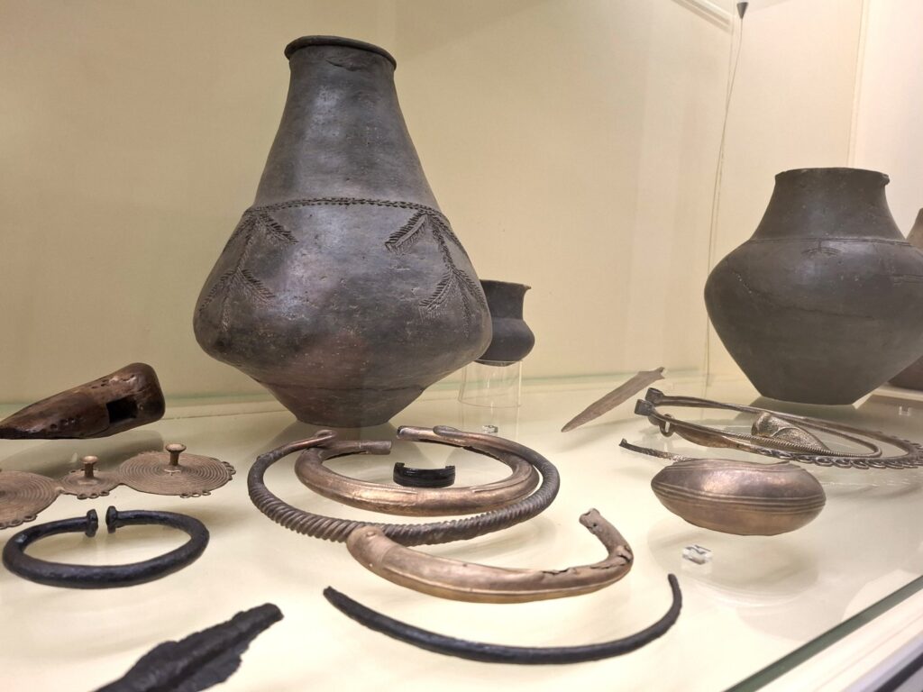 Naczynia ceramiczne oraz metalowe ozdoby prezentowane w gablocie wystawy archeologicznej (kliknięcie powiększy zdjęcie)