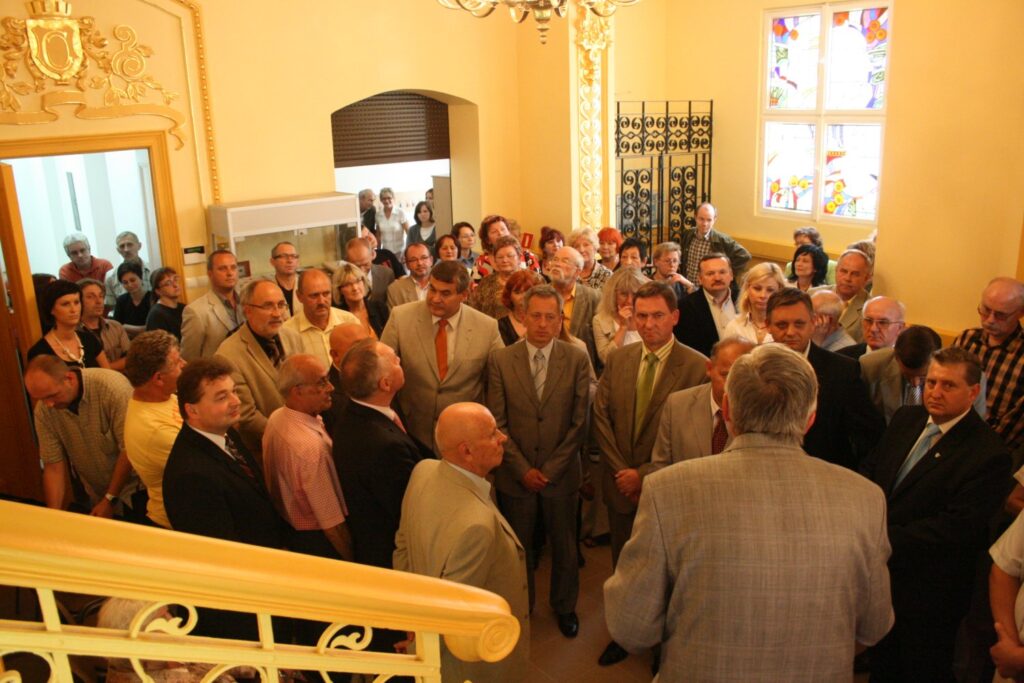 Duża grupa osób zebrana w holu budynku, patrząca w stronę mówiącego mężczyzny stojącego przy balustradzie (kliknięcie powiększy zdjęcie)