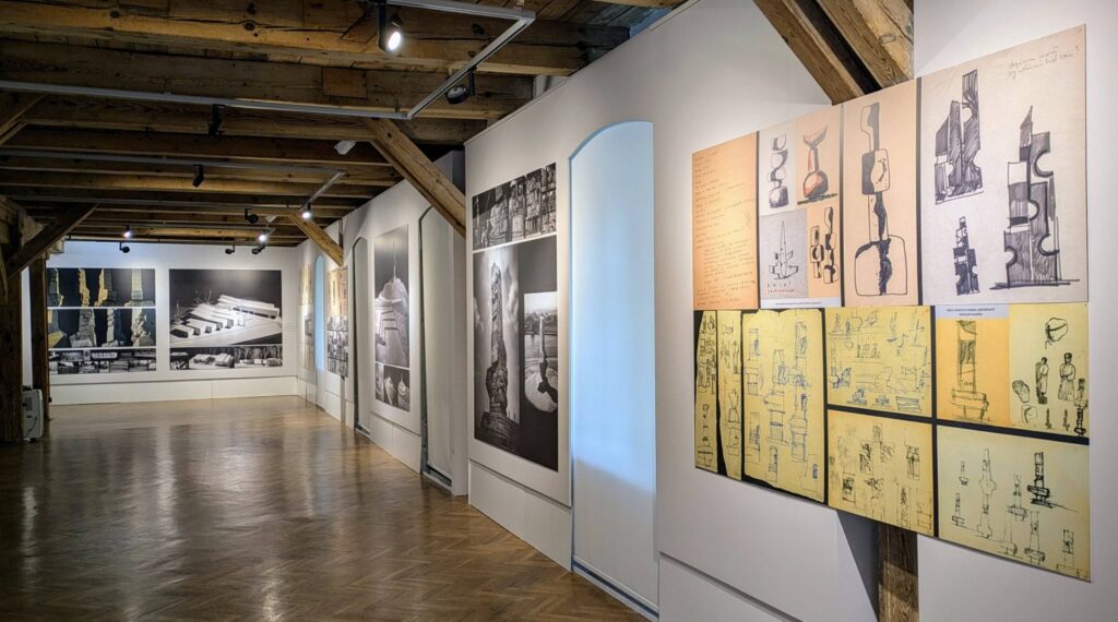 Fragment ekspozycji z rysunkami i projektami na planszach oraz fotografiami archiwalnymi w przestrzeni galerii (kliknięcie powiększy zdjęcie).