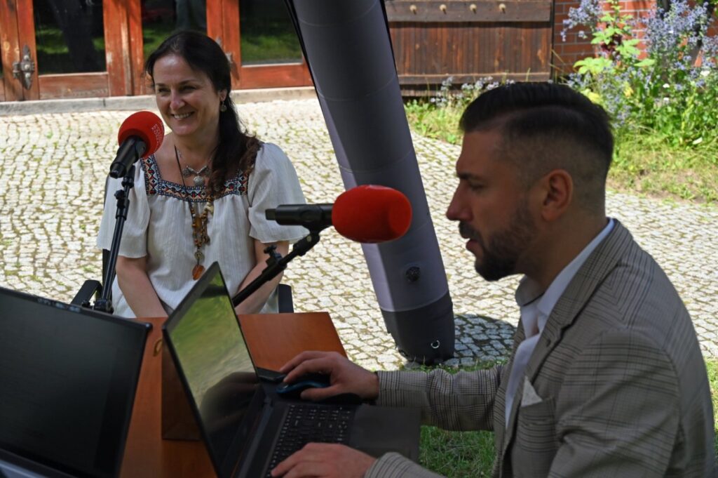 Dwie osoby siedzą przy mikrofonie w studiu plenerowym Radia Koszalin (kliknięcie spowoduje powiększenie zdjęcia).