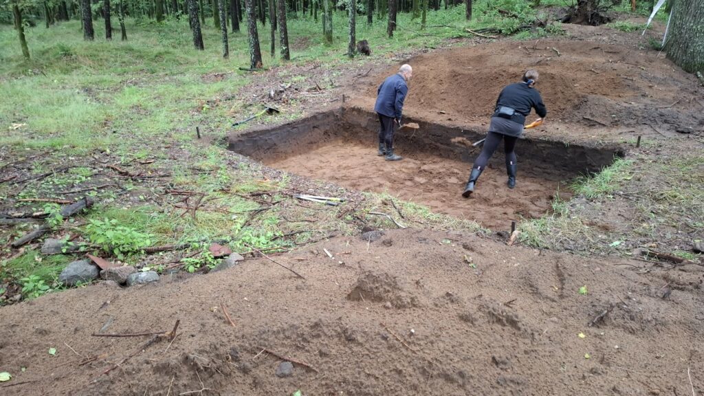 Wykop archeologiczny w lesie, w którym pracują dwie osoby (kliknięcie spowoduje powiększenie zdjęcia).