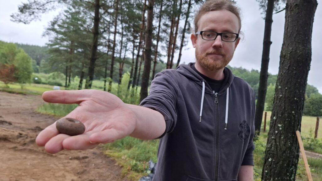 Mężczyzna, na wyciągniętej dłoni, pokazuje ciężarek tkacki (kliknięcie spowoduje powiększenie zdjęcia).