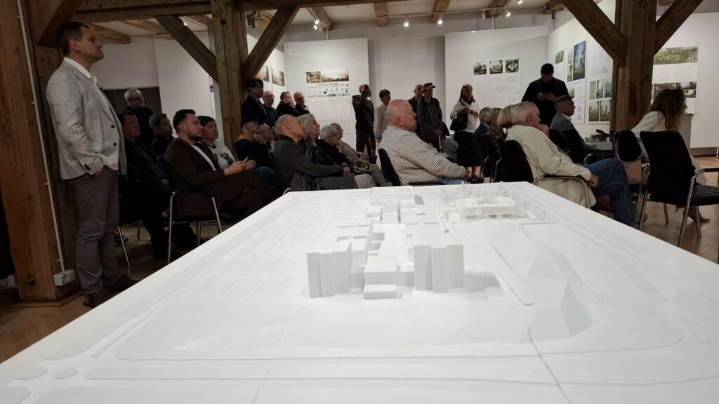 Widok na salę z publicznością oraz makietą architektoniczną na pierwszym planie podczas spotkania (kliknięcie powiększy zdjęcie).