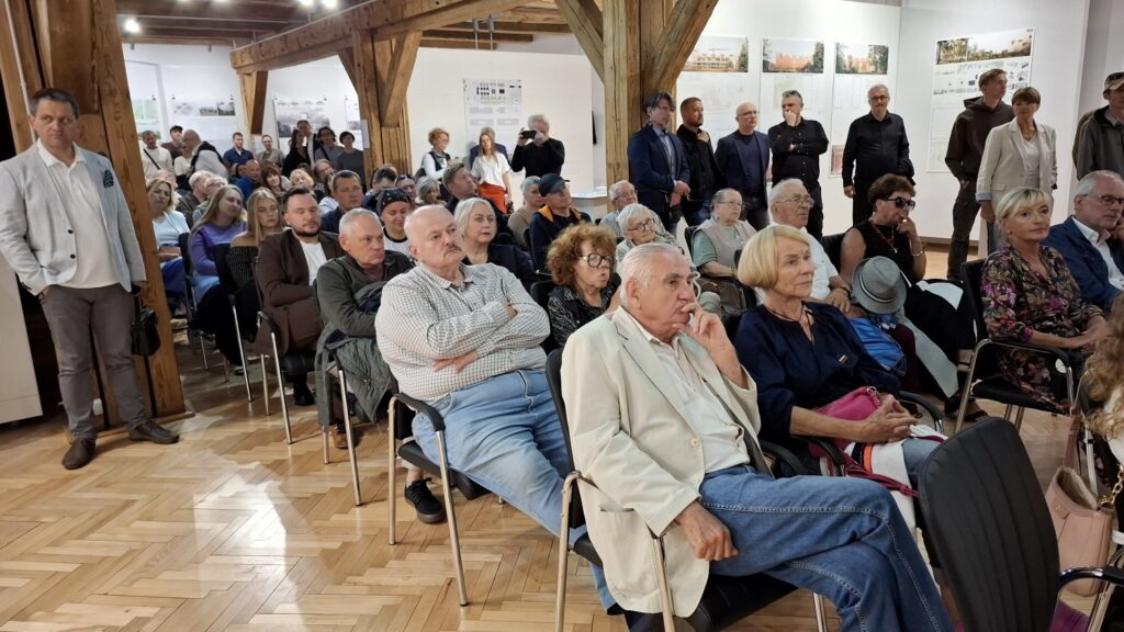 Widok na licznie zgromadzoną publiczność siedzącą i stojącą w sali podczas spotkania lub wykładu (kliknięcie powiększy zdjęcie).