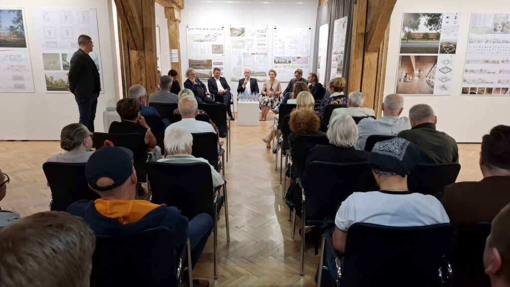 Widok od tyłu na publiczność siedzącą na krzesłach podczas panelu dyskusyjnego w sali wystawowej (kliknięcie powiększy zdjęcie).