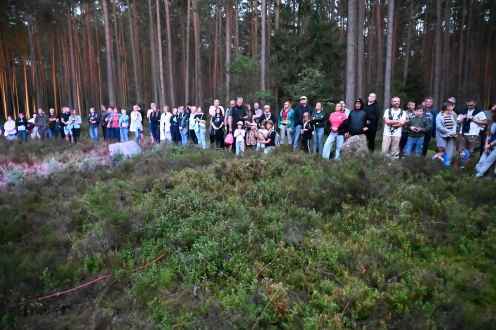 Uczestnicy stoją na skraju polany w lesie, obserwując wydarzenie Nocy Gotów w otoczeniu wrzosowisk (kliknięcie powiększy zdjęcie).