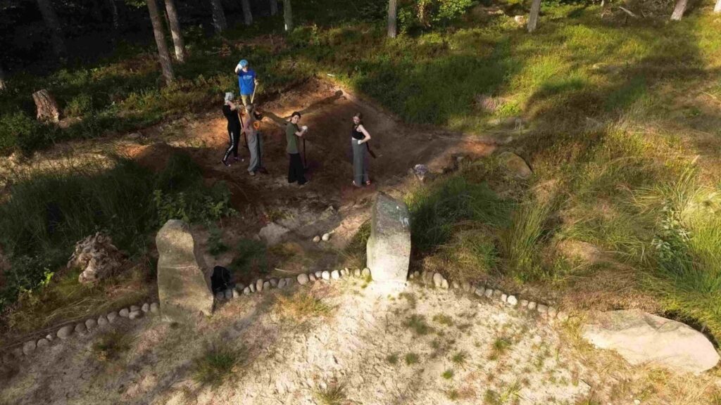 Widok z góry na stanowisko archeologiczne w lesie, grupa osób stoi przy kamiennym kręgu (kliknięcie powiększy zdjęcie).