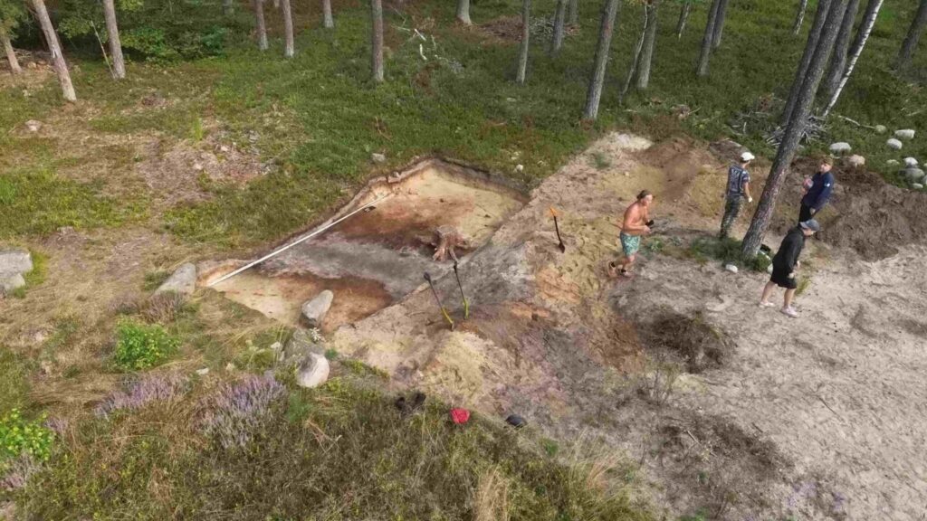 Widok z góry na wykop archeologiczny, kilka osób pracuje przy odsłanianiu warstw ziemi (kliknięcie powiększy zdjęcie).