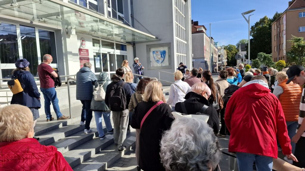 Uczestnicy wydarzenia stoją przy schodach prowadzących do Ratusza i podczas spaceru historycznego (kliknięcie powiększy zdjęcie).