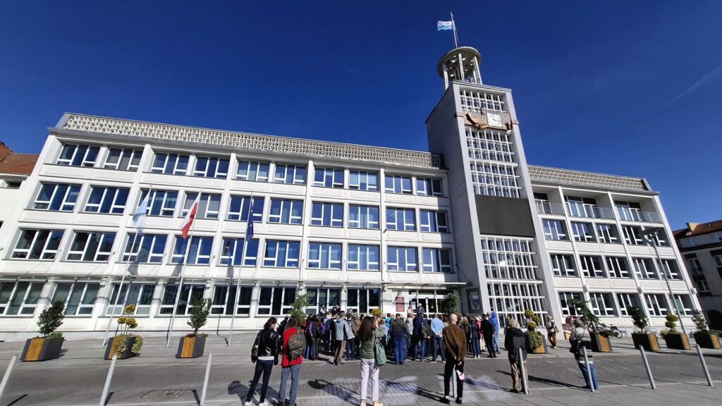 Uczestnicy spotkania na tle budynku Ratusza z wieżą i tarczą zegarową, w tle bezchmurnie niebo (kliknięcie powiększy zdjęcie).