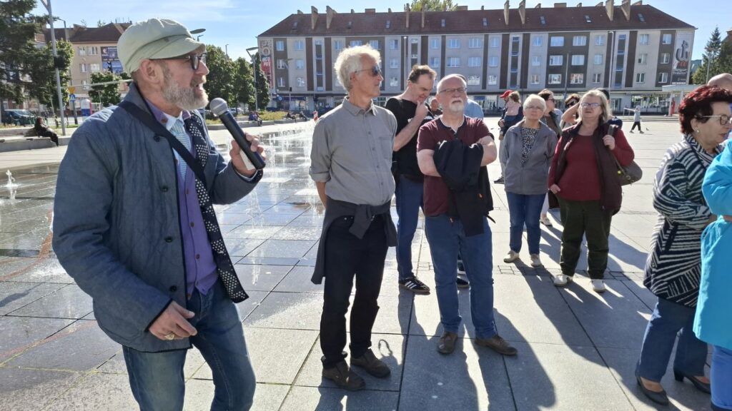 Przewodnik opowiada uczestnikom o historii Ratusza na tle fontanny i zabudowy miejskiej (kliknięcie powiększy zdjęcie).