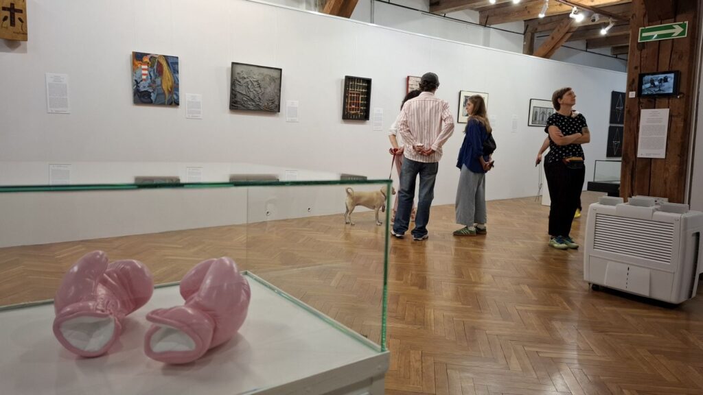 Osoby oglądają wystawę w przestronnej sali galerii, na pierwszym planie gabloty z eksponatami (kliknięcie powiększy zdjęcie).