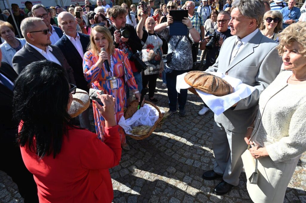 Przemówienie podczas otwarcia wydarzenia, uczestnicy trzymają tradycyjny chleb (kliknięcie powiększy zdjęcie).