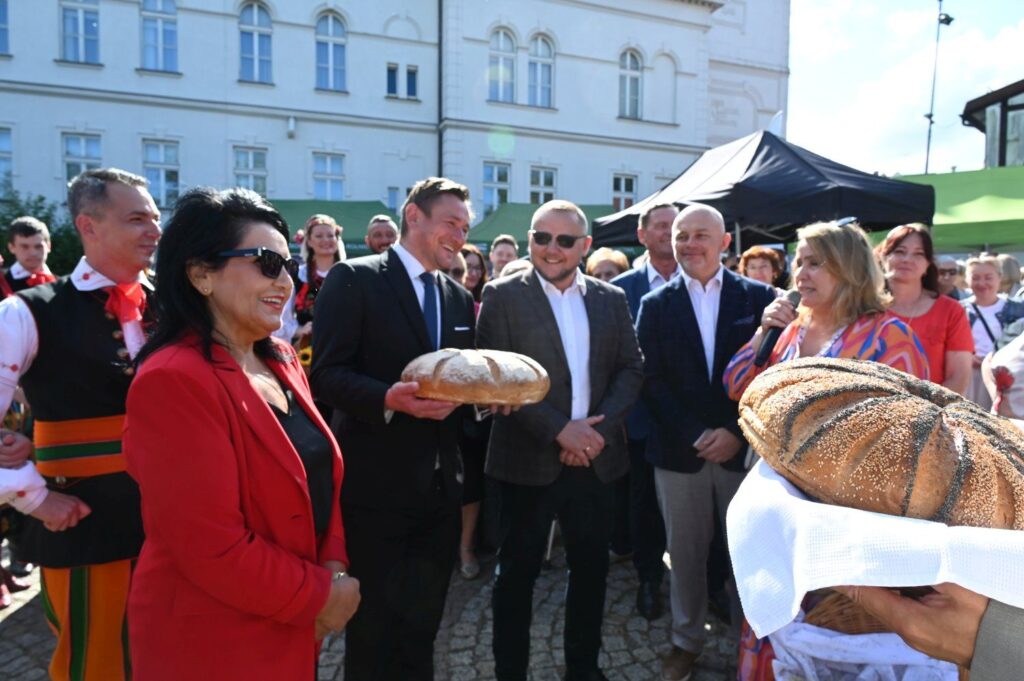 Uczestnicy festynu dożynkowego zgromadzeni wokół ceremonii przekazania chleba, widoczny tłum i stoiska (kliknięcie powiększy zdjęcie).