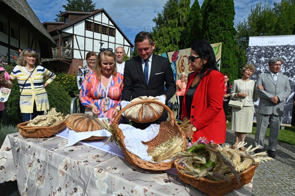Prezentacja tradycyjnych bochnów chleba i wieńców dożynkowych na stole podczas uroczystości plenerowej (kliknięcie powiększy zdjęcie).