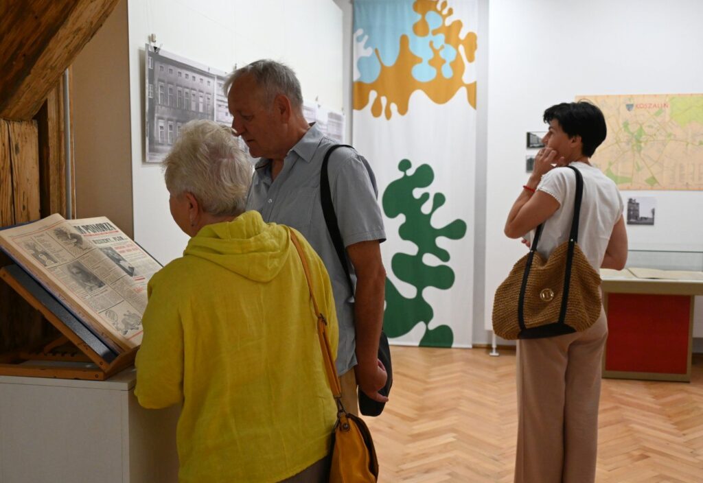 Zwiedzający czytający materiały archiwalne prezentowane na pulpicie wystawowym w muzeum (kliknięcie powiększy zdjęcie).