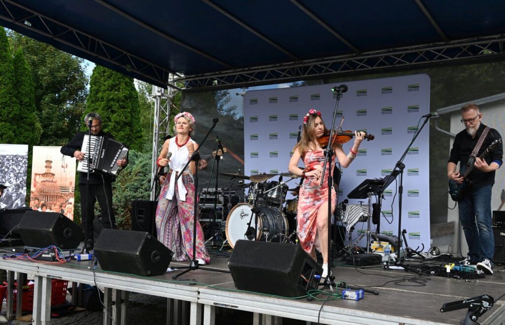 Zespół muzyczny grający koncert na scenie, wokalistka i instrumentalistka na pierwszym planie (kliknięcie powiększy zdjęcie).