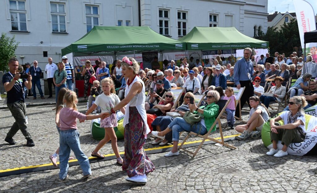 Kobieta tańcząca z dziećmi przed sceną podczas koncertu, wokół siedzący uczestnicy wydarzenia (kliknięcie powiększy zdjęcie).