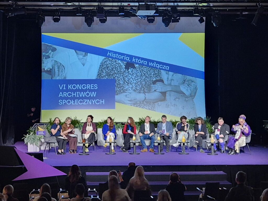 Panel dyskusyjny podczas VI Kongresu Archiwów Społecznych – uczestnicy siedzą na scenie przed dużym ekranem z napisem „Historia, która włącza” (kliknięcie powiększy zdjęcie).