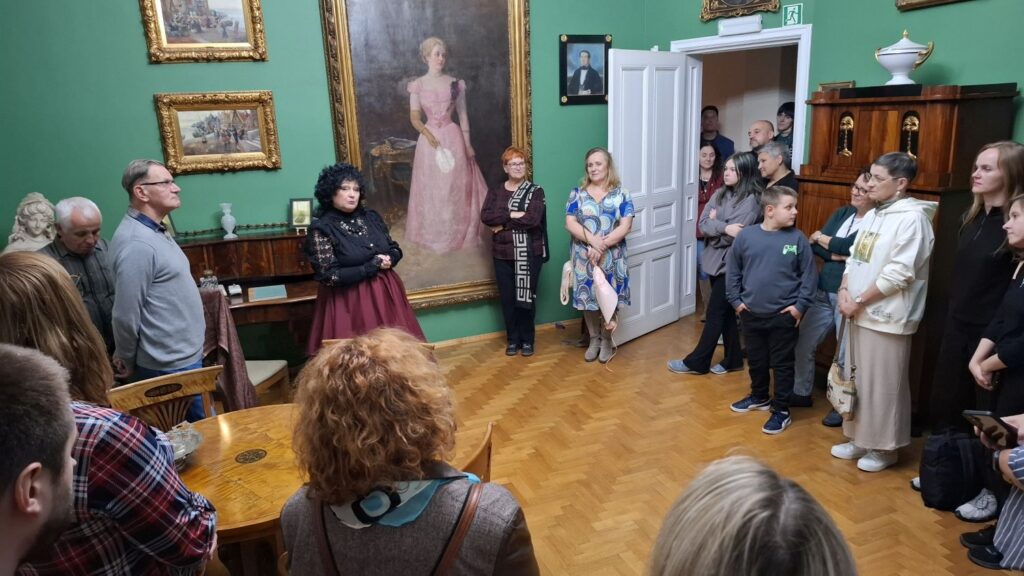 Uczestnicy zwiedzania stoją w sali z portretami i zabytkowymi meblami słuchając opowieści o sztuce dawnej (kliknięcie powiększy zdjęcie).