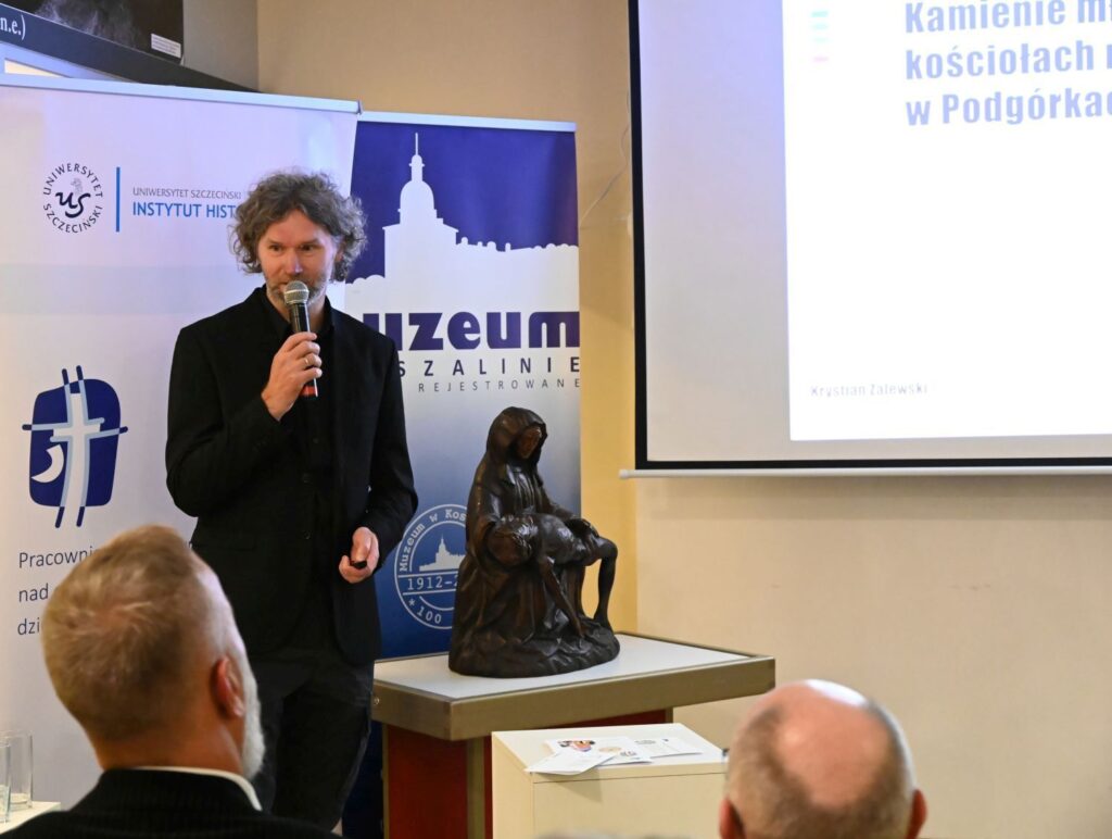 Prelegent prowadzi wykład przy ekranie z prezentacją w sali muzealnej (kliknięcie powiększy zdjęcie).