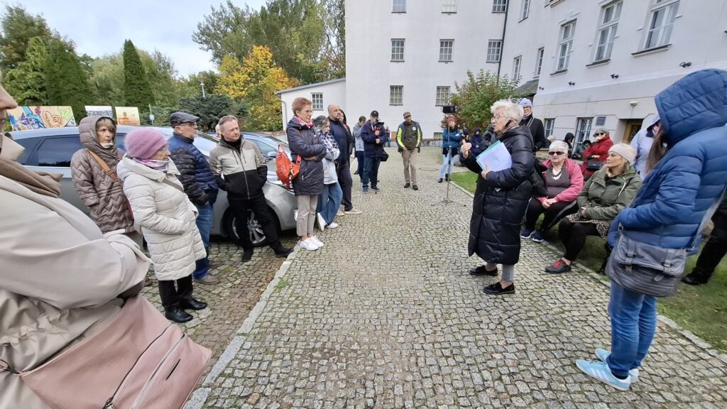 Uczestnicy spaceru historycznego stoją na muzealnym dziedzińcu i słuchają przewodnika podczas zwiedzania (kliknięcie powiększy zdjęcie).