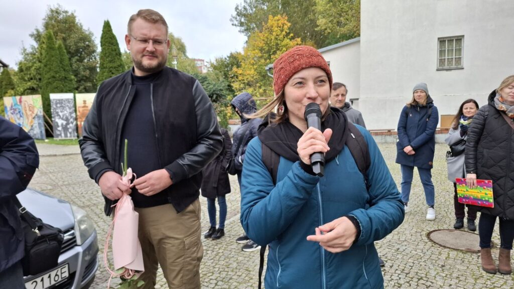 Kobieta trzyma mikrofon i przemawia do uczestników zgromadzonych na dziedzińcu (kliknięcie powiększy zdjęcie).