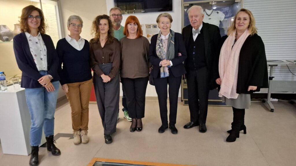 Osiem osób, organizatorzy i prelegenci, pozuje do wspólnego zdjęcia na tle części ekspozycji wystawy archeologicznej (kliknięcie powiększy zdjęcie).