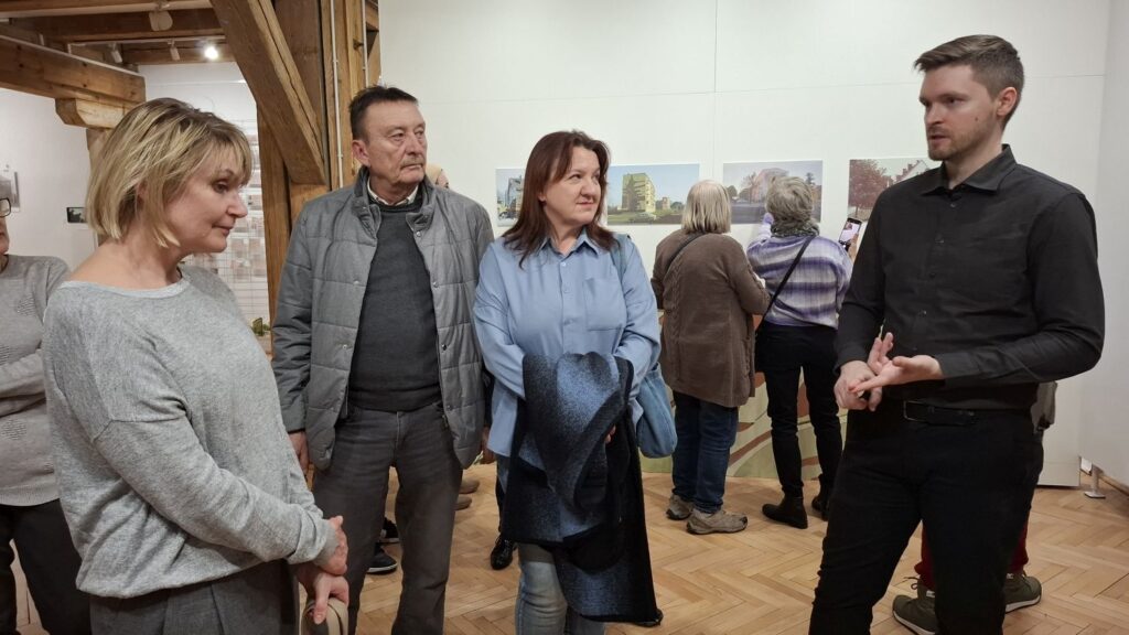 Jeden z kuratorów wystawy rozmawia z uczestnikami oprowadzania po wystawie, stojąc wśród zwiedzających w sali wystawowej (kliknięcie powiększy zdjęcie).