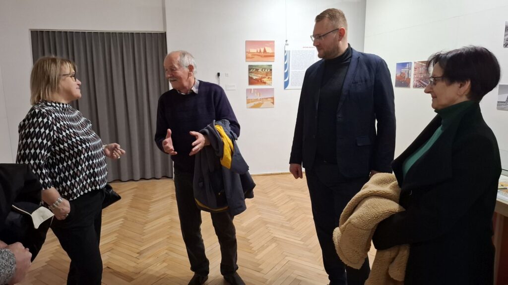 Grupa osób rozmawia ze sobą w sali muzealnej i słucha wspomnień świadka historii związanych Dożynkami Centralnymi w Koszalinie (kliknięcie powiększy zdjęcie).