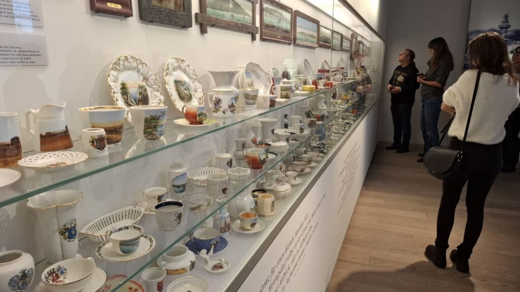 Długa gablota z porcelaną i naczyniami użytkowymi, oglądana przez zwiedzających w jasnej sali muzeum (kliknięcie powiększy zdjęcie)