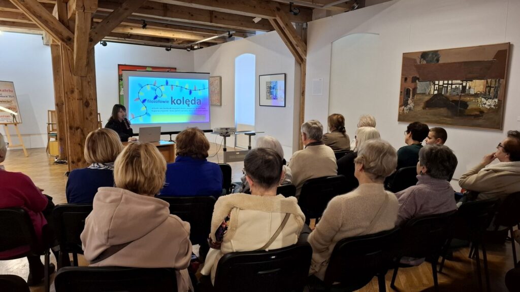 Uczestnicy siedzący na krzesłach oglądają prezentację multimedialną podczas wykładu w przestrzeni muzeum (kliknięcie powiększy zdjęcie)