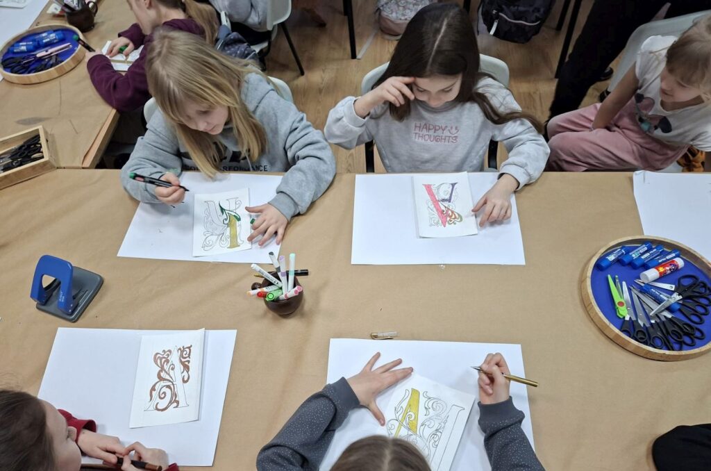 Dzieci siedzą przy stołach i kolorują dekoracyjne wzory przygotowane na zajęcia walentynkowe (kliknięcie powiększy zdjęcie).