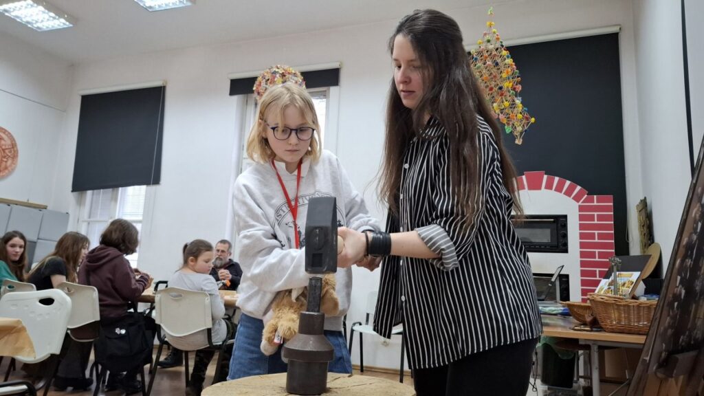 Dziewczynka wraz z prowadzącą wybija wzór na metalowym krążku przy użyciu stempla i młota podczas warsztatów mincerskich (kliknięcie powiększy zdjęcie).