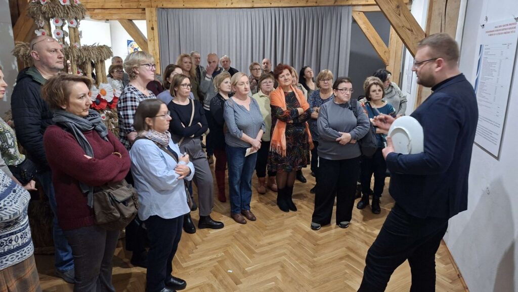 Grupa uczestników oprowadzania stoi w sali wystawowej i słucha kuratora wystawy opowiadającego o wystawie (kliknięcie powiększy zdjęcie).