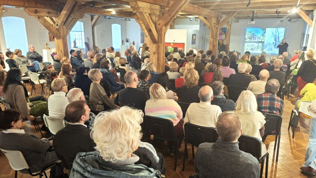 Widok sali wypełnionej publicznością podczas wykładu o twórczości Caspara Davida Friedricha, z drewnianą konstrukcją wnętrza i ekranem projekcyjnym w tle (kliknięcie powiększy zdjęcie).
