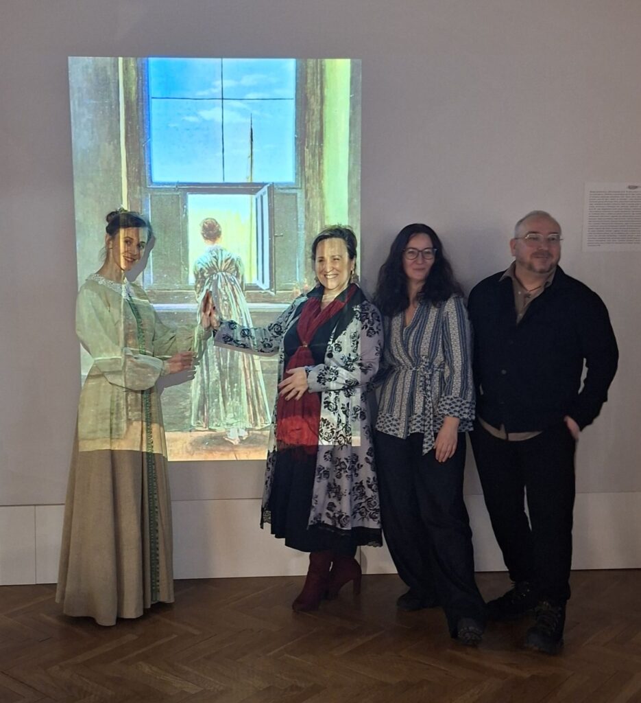 Czworo uczestników wydarzenia stoi przed projekcją obrazu „Kobieta w oknie” Caspara Davida Friedricha, pozując do wspólnego zdjęcia w przestrzeni sali wystawowej (kliknięcie powiększy zdjęcie).