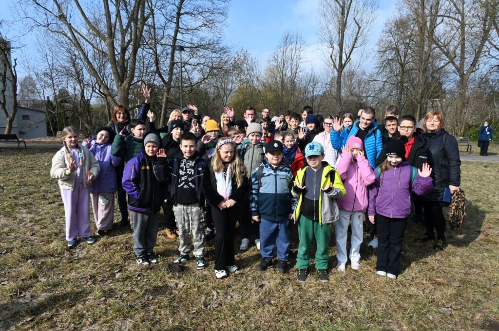 Grupa dzieci i dorosłych pozuje do wspólnego zdjęcia na terenie zielonym podczas wydarzenia (kliknięcie powiększy zdjęcie).