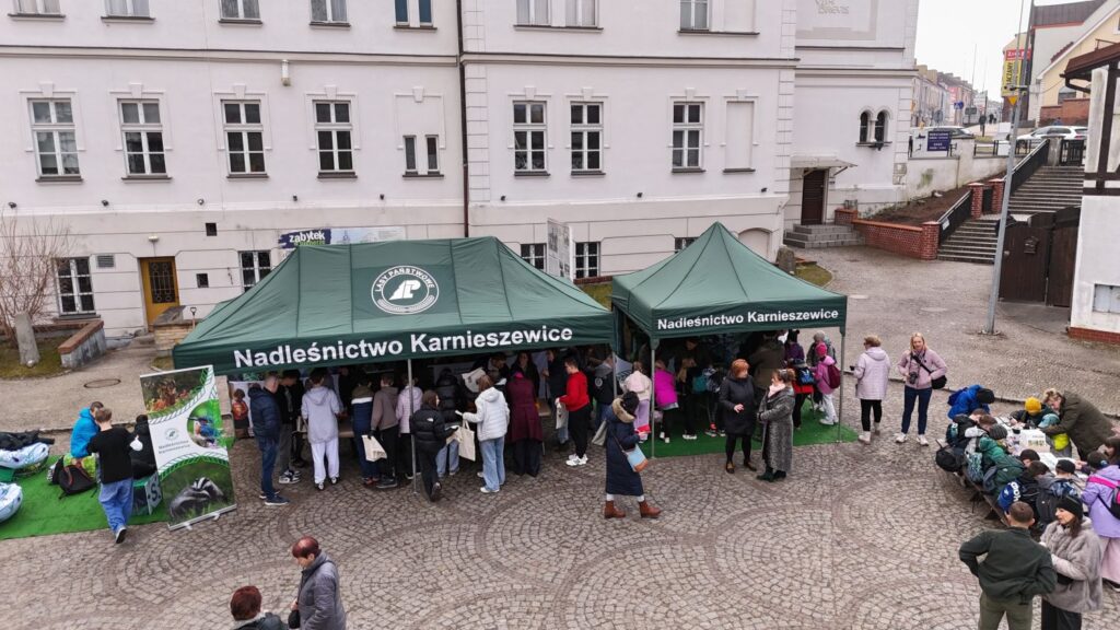 Uczestnicy zgromadzeni wokół namiotu warsztatowego na dziedzińcu muzeum podczas wydarzenia plenerowego, na drugim planie zabudowania muzeum (kliknięcie powiększy zdjęcie).