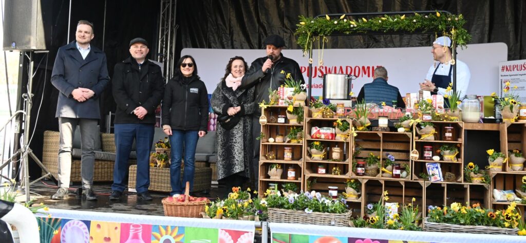 Scena kiermaszu z dekoracjami wielkanocnymi, na scenie stoją organizatorzy i otwierają wydarzenie (kliknięcie powiększy zdjęcie).