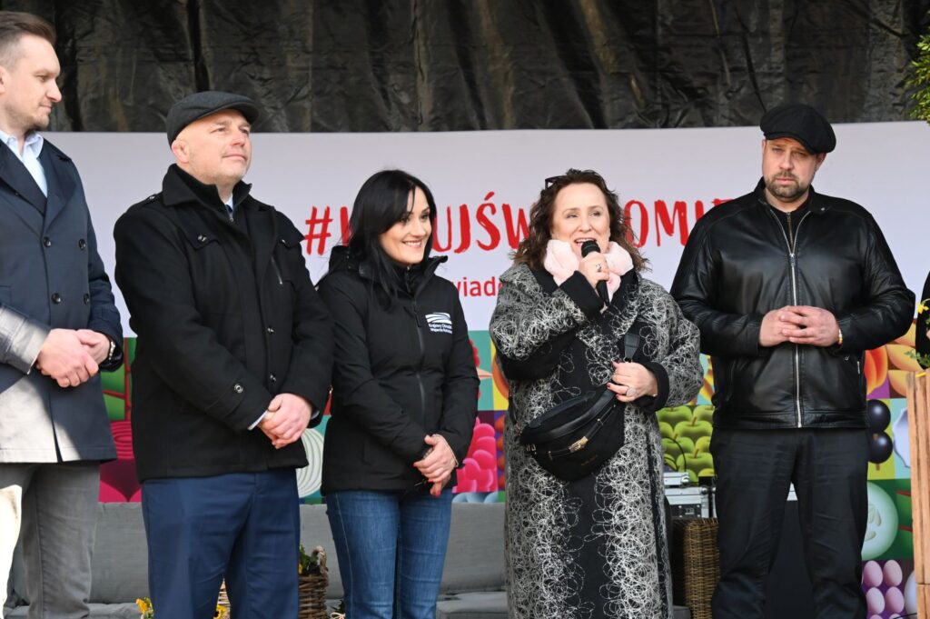 Organizatorzy kiermaszu wielkanocnego na scenie, kobieta przemawia do mikrofonu, obok niej stoją pozostali goście (kliknięcie powiększy zdjęcie).