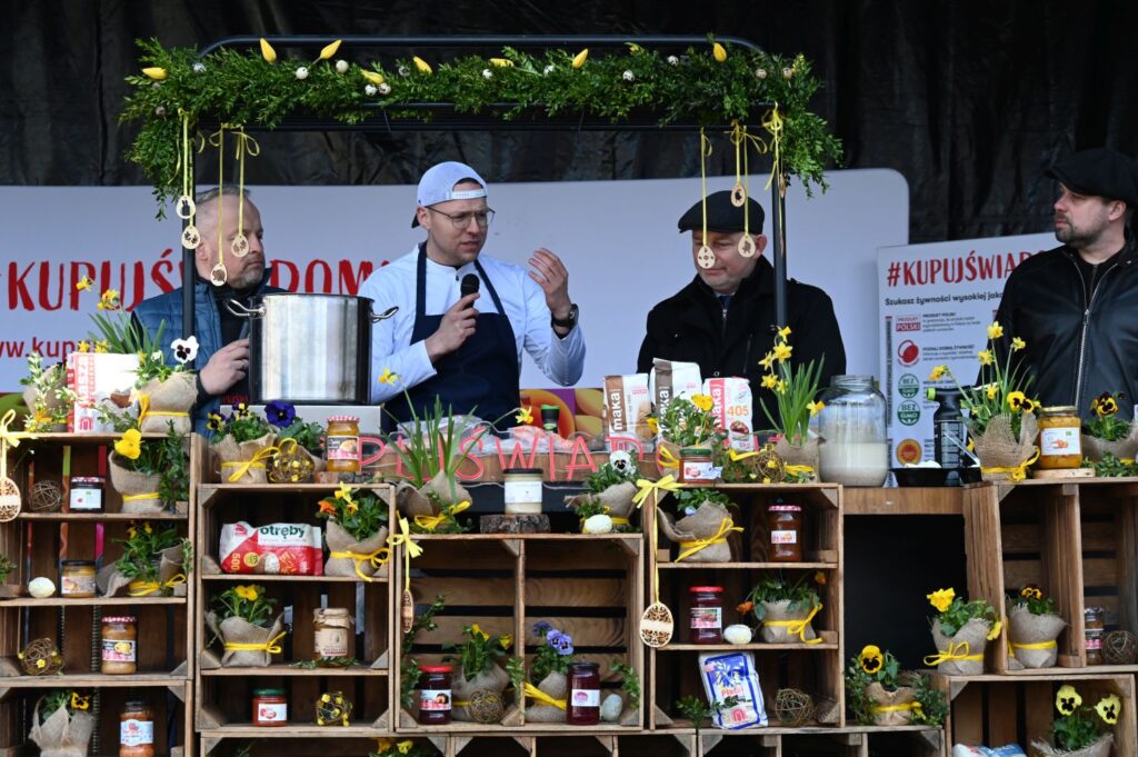 Kucharz prowadzi pokaz kulinarny na scenie, przygotowując potrawę wśród wielkanocnych dekoracji (kliknięcie powiększy zdjęcie).