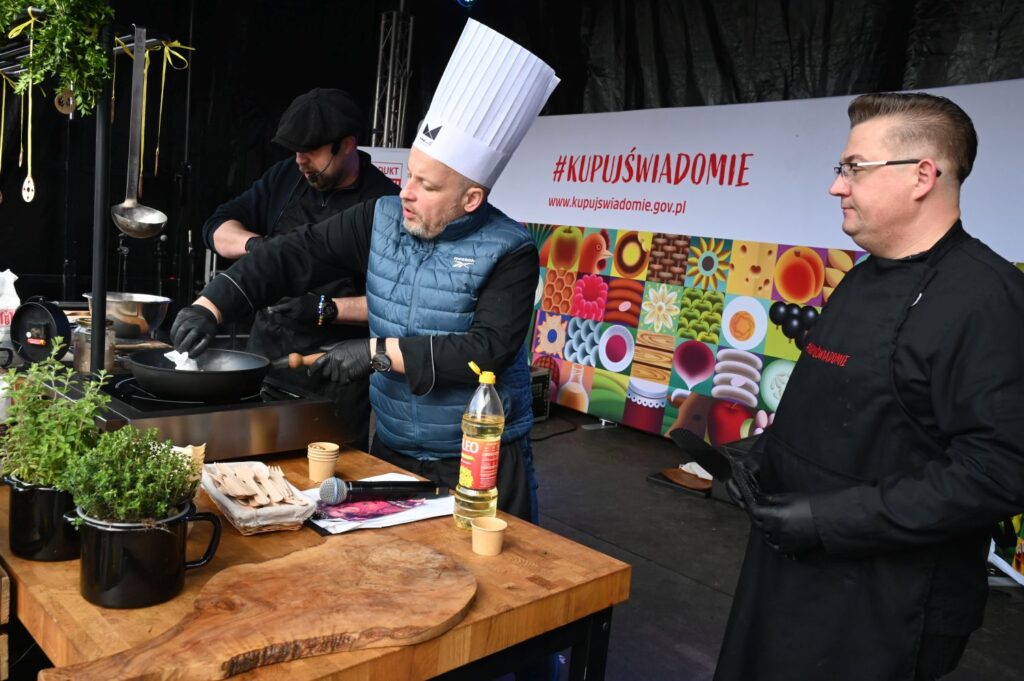 Kucharze wspólnie przygotowują danie na patelni podczas pokazu kulinarnego na scenie (kliknięcie powiększy zdjęcie).