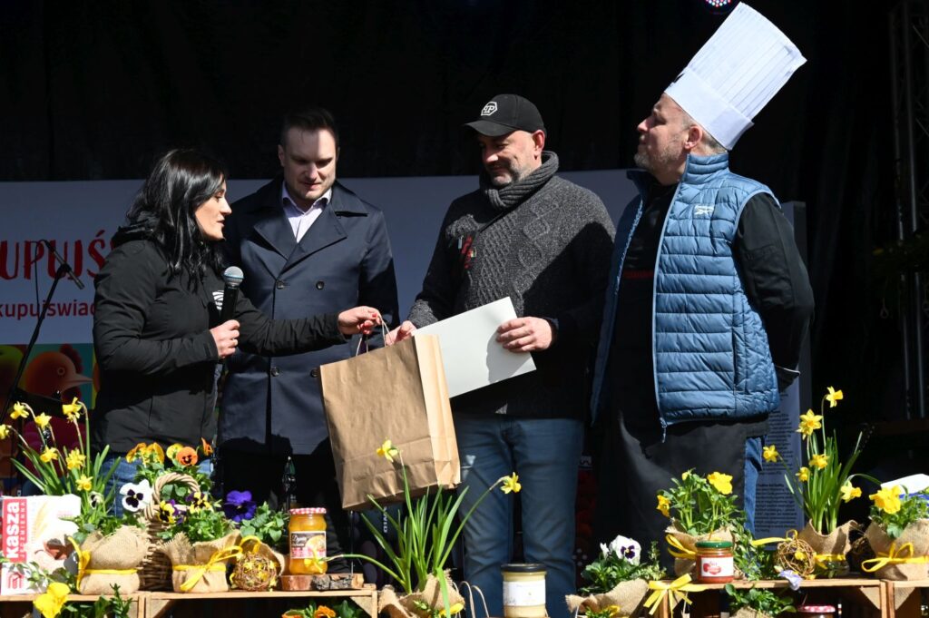 Uczestnicy konkursu odbierają nagrody i upominki na scenie wśród dekoracji wiosennych (kliknięcie powiększy zdjęcie).