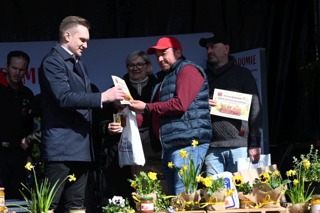 Uczestnik w czerwonej czapce odbiera nagrodę z rąk organizatora konkursu (kliknięcie powiększy zdjęcie).
