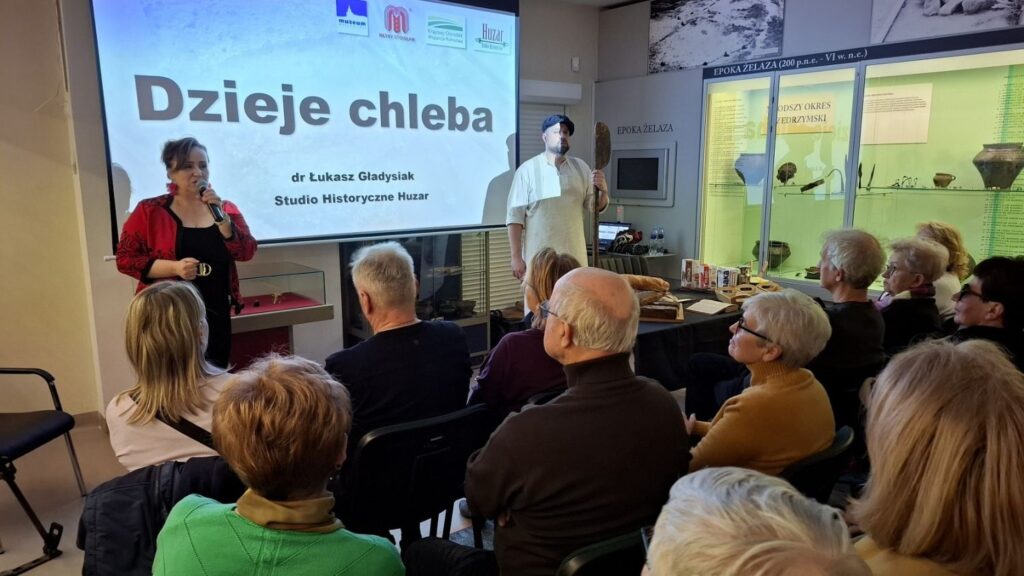 Prelekcja o dziejach chleba prowadzona przed publicznością, z prezentacją wyświetlaną na ekranie (kliknięcie powiększy zdjęcie).