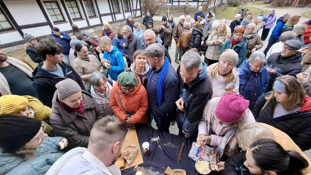 Liczna grupa osób otacza stół na zewnątrz, biorąc udział w degustacji i pokazie związanym z chlebem (kliknięcie powiększy zdjęcie).