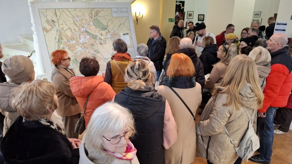 Grupa zwiedzających gromadzi się wokół planszy z mapą, słuchając komentarza prowadzącego (kliknięcie powiększy zdjęcie).