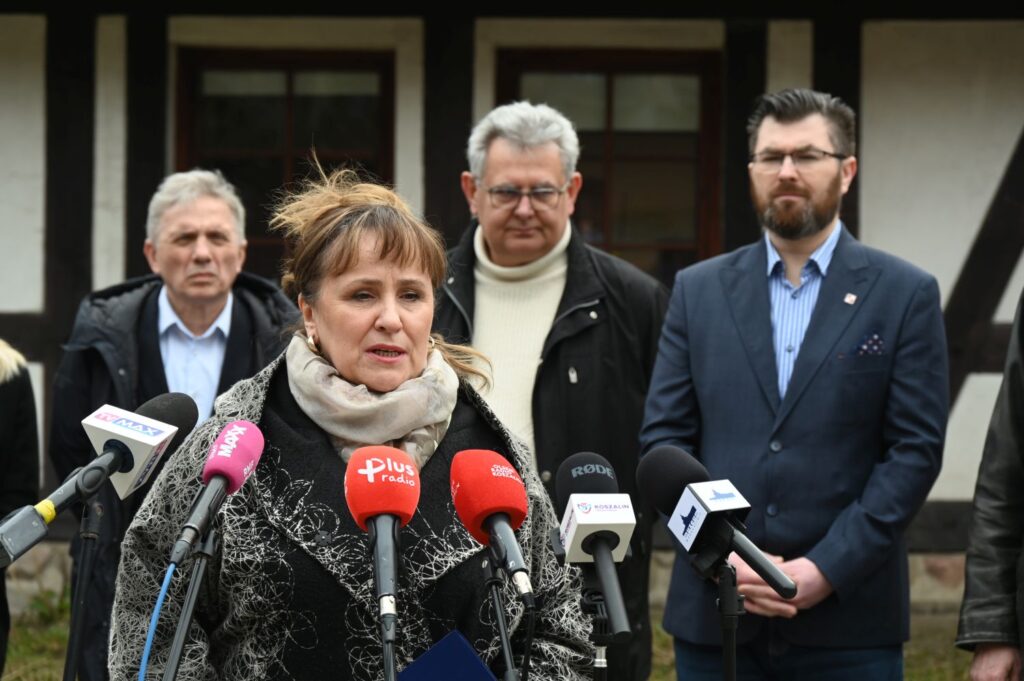 Dyrektor Muzeum w Koszalinie stoi przed mikrofonami i przemawia w trakcie konferencji prasowej, w tle fragment budynku administracji (kliknięcie powiększy zdjęcie).