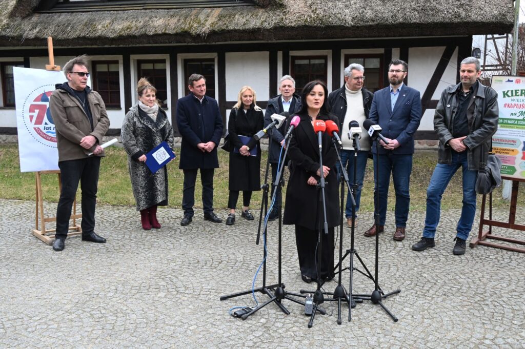 Kobieta przemawia do osób zgromadzonych na konferencji prasowej, za nią stoją wszyscy zaproszeni na konferencję goście (kliknięcie powiększy zdjęcie).